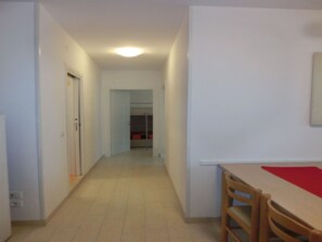 A narrow hallway with a wooden table and chairs, a door on the left, and a closet in the background.
