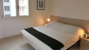 A bedroom with a bed, a nightstand, a framed picture on the wall, and a window with a view of a building. - Lovely Flat Close to the Beach-beahost (San Michele al Tagliamento)