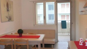 A room with a dining table, chairs, a sofa, a potted plant, and a window with a view of a balcony. - Lovely Flat Close to the Beach-beahost (San Michele al Tagliamento)