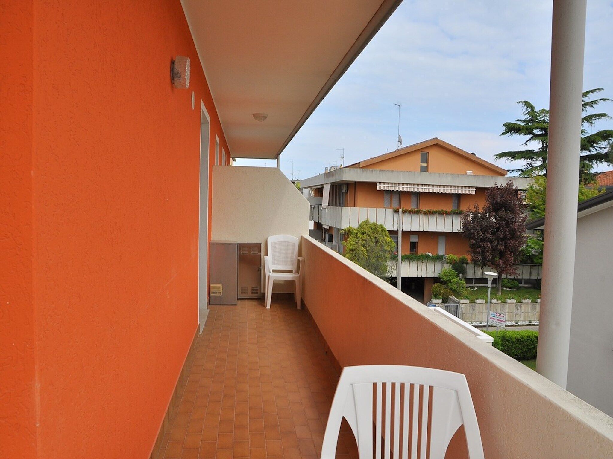 A narrow balcony with a white chair, a small table, and a heater.