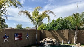 Ein Swimmingpool mit klarem Wasser, umgeben von einer Backsteinmauer, Palmen und zwei amerikanischen Flaggen.