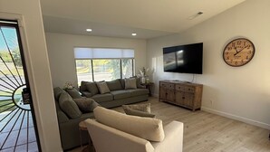 Ein modernes Wohnzimmer mit einem beigen Sofa, einem Holzschrank und einem flachbildfernseher an der Wand.