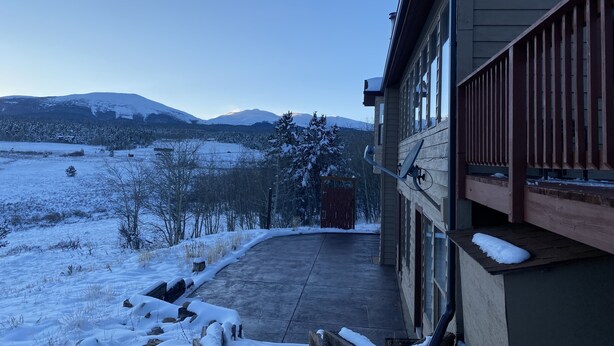 Una casa con porche cubierto y vistas a montañas nevadas bajo un cielo despejado.