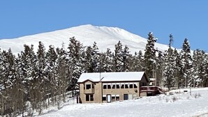 Paisaje nevado con un edificio que cuenta con una amplia sección de ventanas y una terraza de madera.