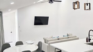 A modern kitchen with a dining area, white cabinetry, a ceiling fan, pendant lights, and a flat-screen TV. - Luxury Villa w/ pool wef/polo 5 min (Wellington)