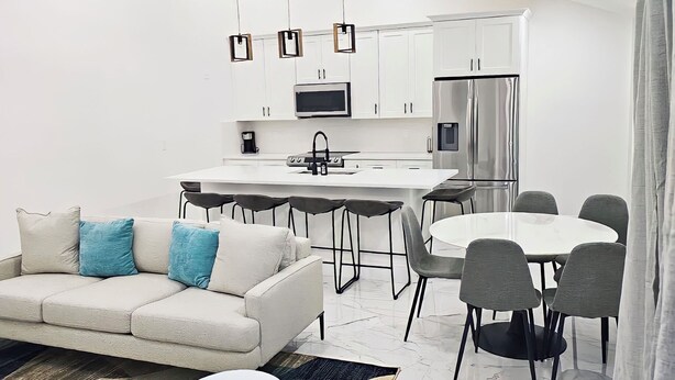 A modern kitchen with white cabinets, a stainless steel refrigerator, and a dining area with a white table and grey chairs. - Luxury Villa w/ pool wef/polo 5 min (Wellington)