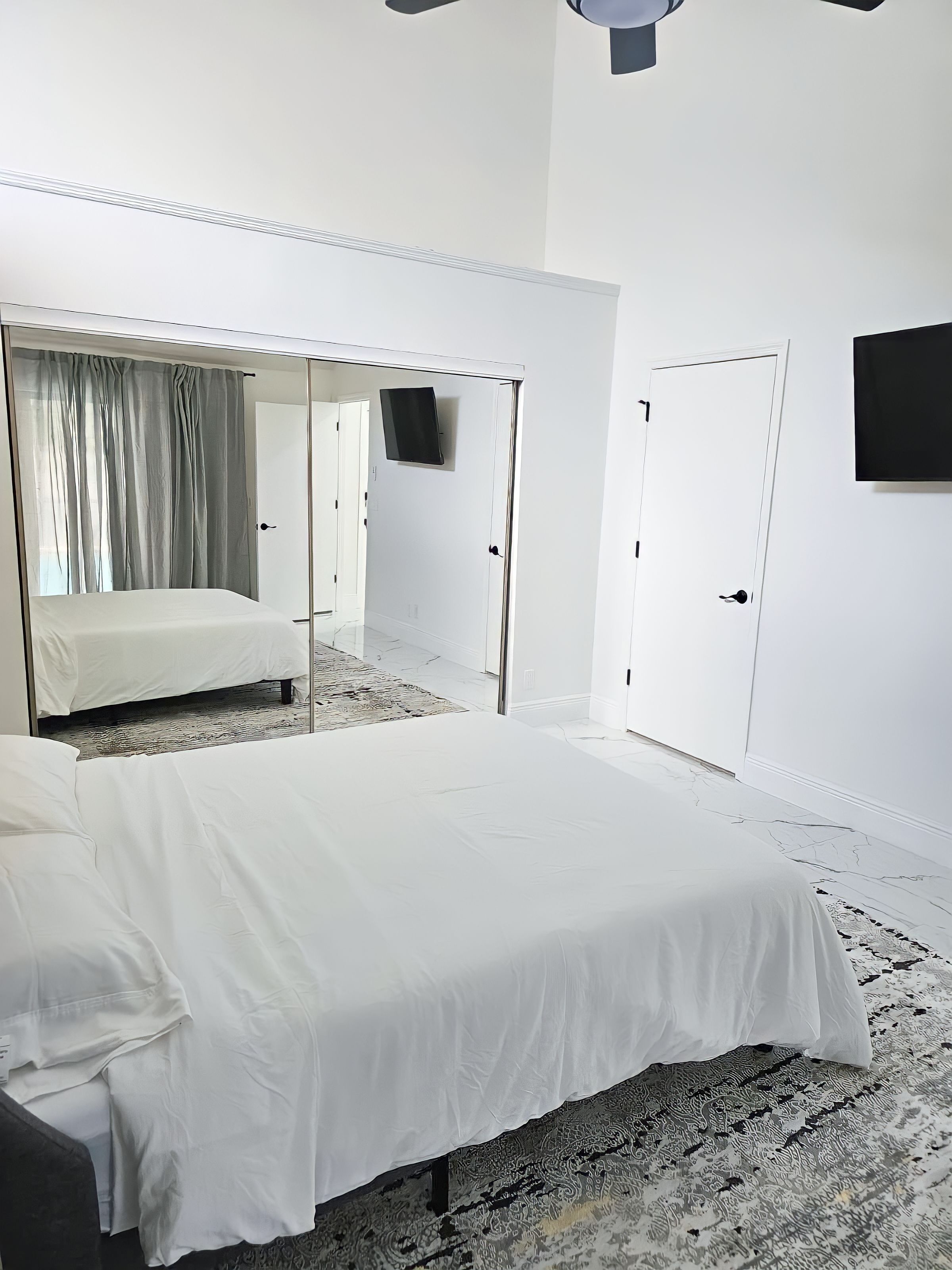 Habitación de hotel con una cama grande, una cama más pequeña, un televisor de pantalla plana montado en la pared y un armario con espejo.