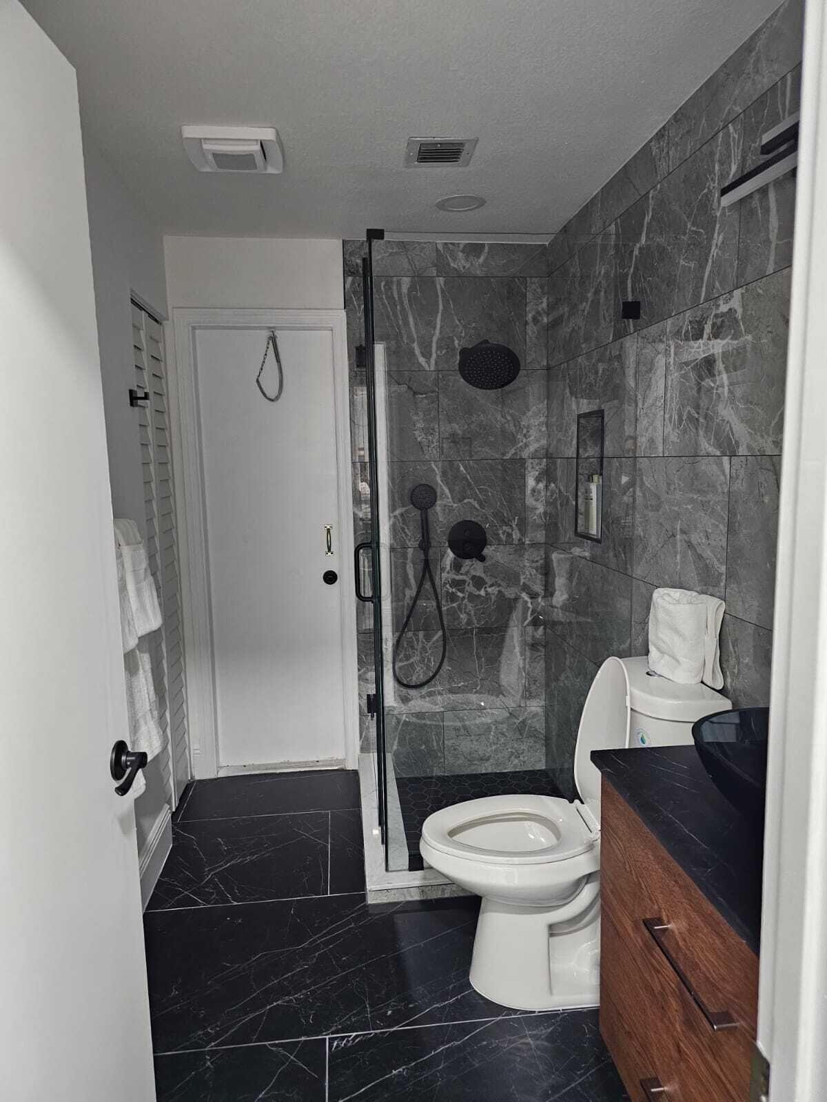 Un baño moderno con ducha de vidrio, inodoro blanco y tocador de madera.