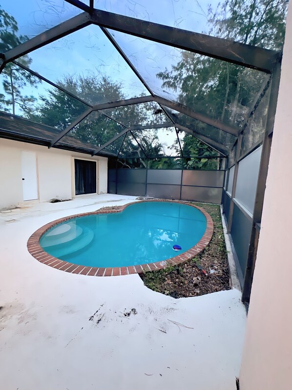 Una piscina techada con borde de ladrillo, rodeada por un suelo de madera blanco y una cerca de metal.