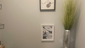 A bathroom with a toilet, a framed picture, a vase with green plants, and a small metal stool. - Amazing Event Space with Ample Parking  (Marietta)
