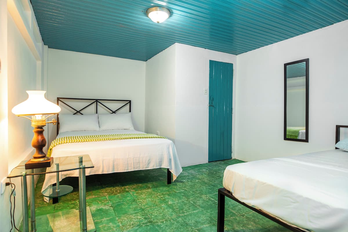 Una habitación con dos camas, una mesita de noche con lámpara, una puerta y un espejo.