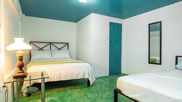 A room with two beds, a nightstand with a lamp, a door, and a mirror.