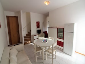 Un espace de vie compact comprenant une table à manger, des chaises, un canapé, un coin cuisine avec un réfrigérateur et un escalier menant à un autre niveau.