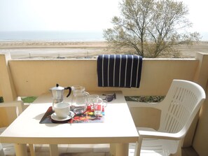 Un tavolo con una macchina da caffè, tazze e un boccale su un balcone con vista sulla spiaggia.