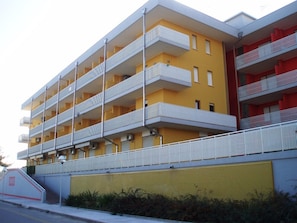 A multi-story building with balconies, a yellow facade, and a gated entrance.