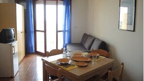 A dining area with a table set for four, a sofa, a television, and a window with blue curtains. - Two Level Attic With sea View Terrace (San Michele al Tagliamento)