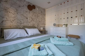 Ein Schlafzimmer mit Bett, Schminktisch, Nachttisch und einer Wand mit Blumenmuster.
