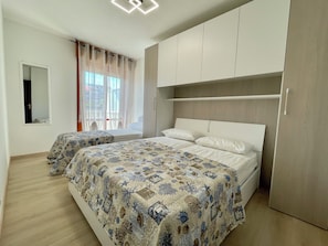 A bedroom with two beds, a wardrobe, a mirror, and a window with curtains. - Apartment for six With Shared Pool (Caorle)