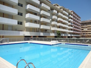Un hotel de varios pisos con balcones, una piscina y cielo despejado.