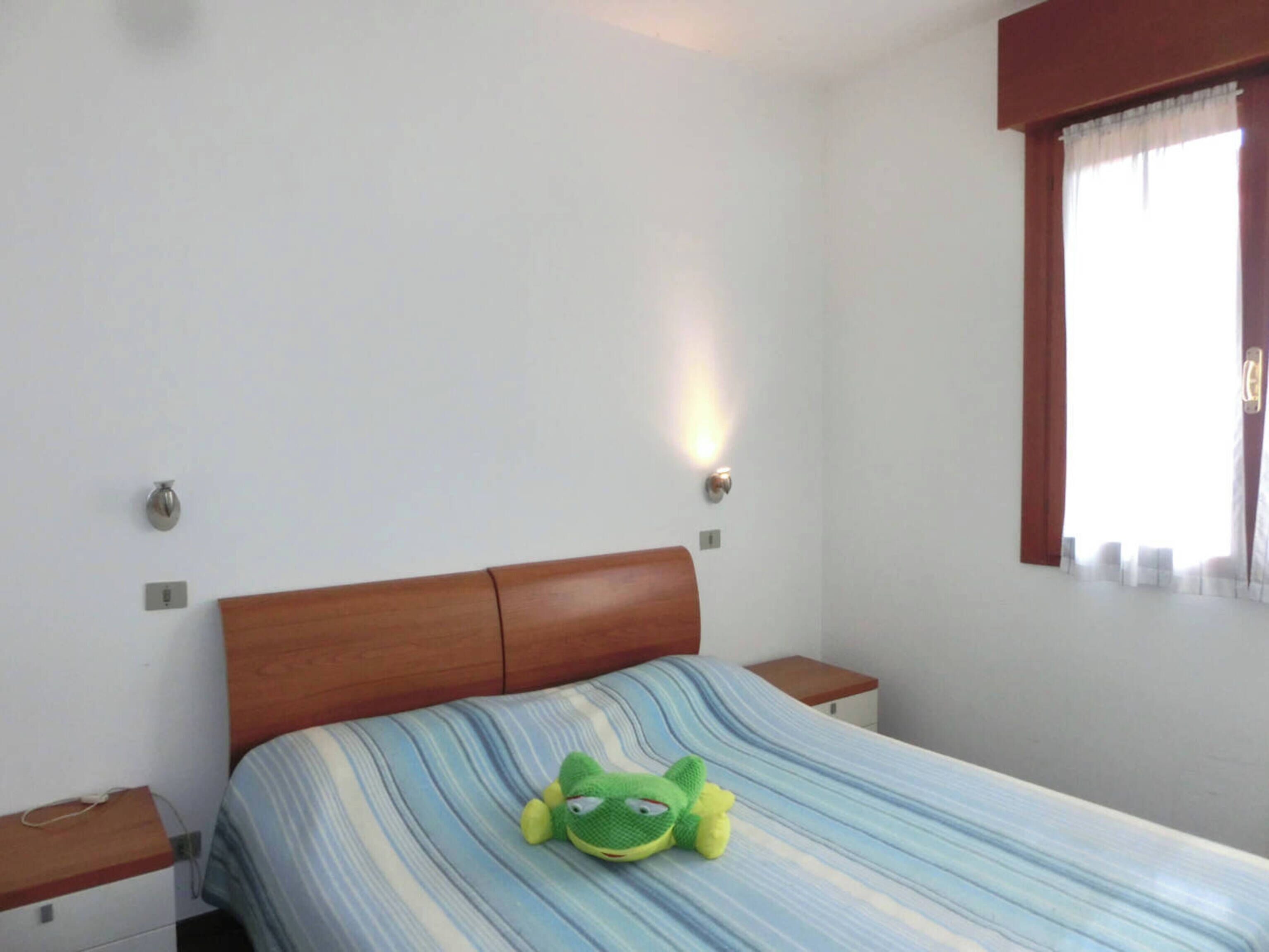 Quarto com cama, mesa de cabeceira, luminária na parede e janela com cortinas.