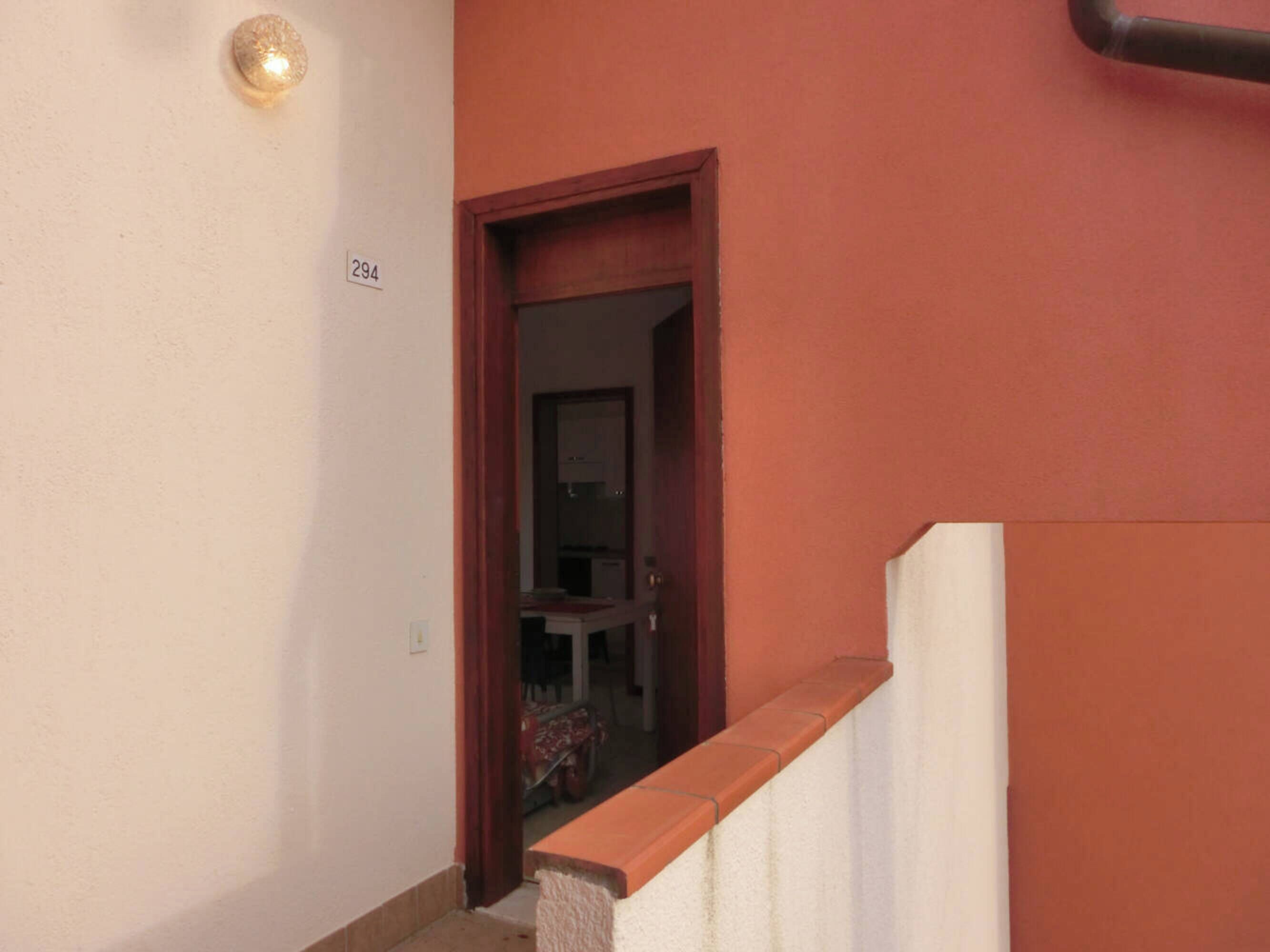 A narrow hallway with a door leading to a room. A small light fixture is mounted on the wall above the door.