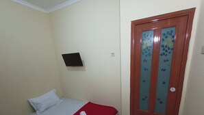 Una habitación pequeña y ordenada con una cama individual, una silla, un televisor montado en la pared y una puerta con un panel de vidrio esmerilado.