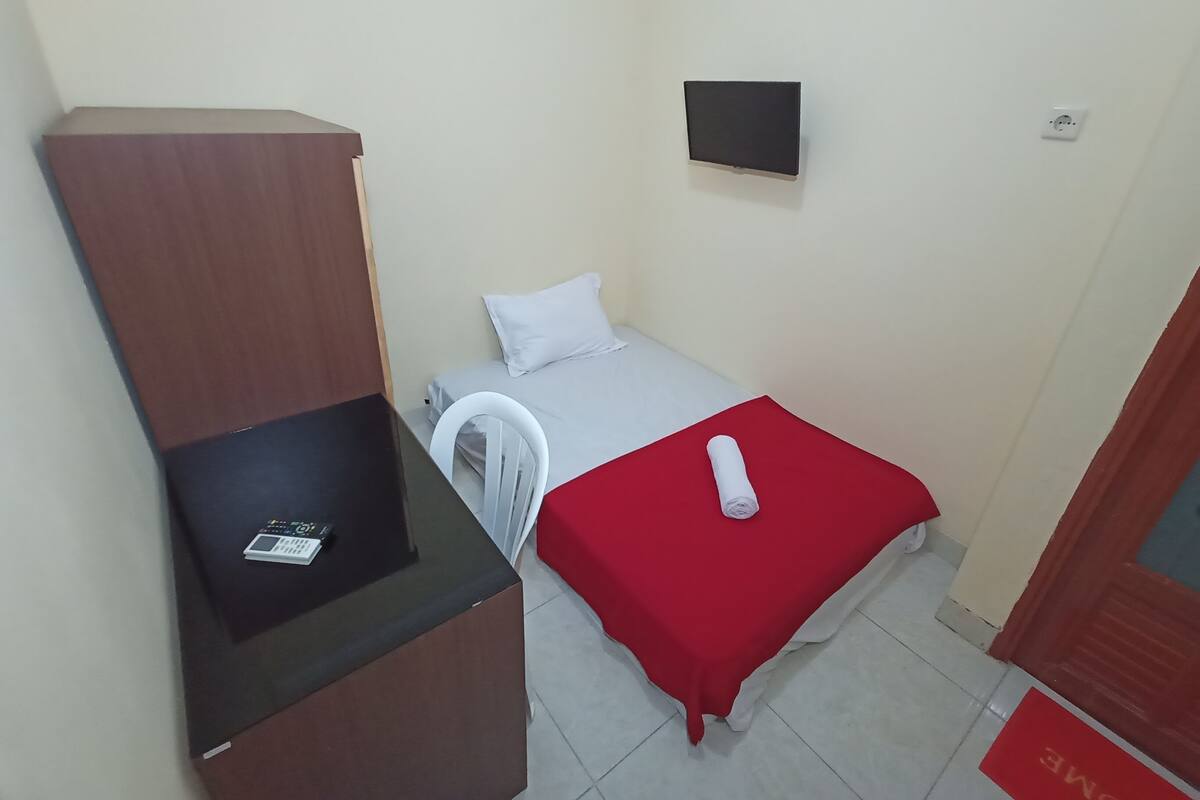 A small, compact room with a single bed, a desk with a chair, and a TV mounted on the wall.