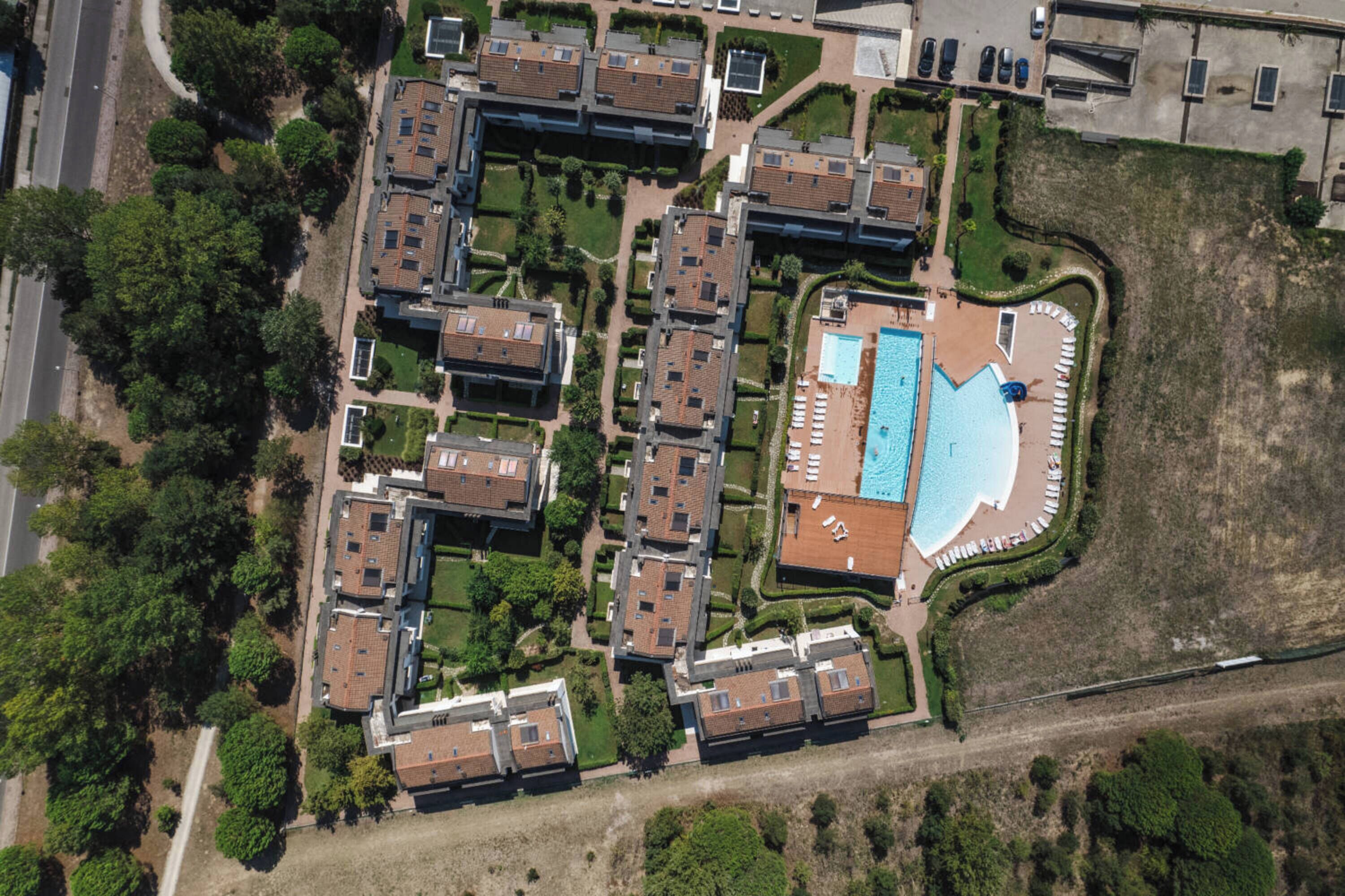 Vista aérea de un complejo residencial con varios edificios de apartamentos, una piscina y un estacionamiento.