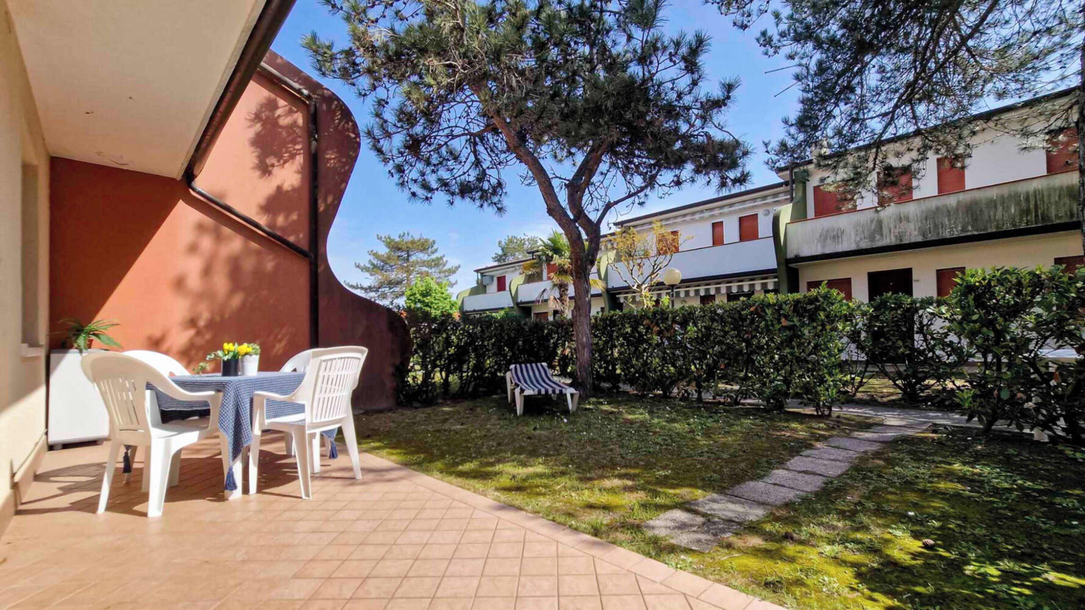 A courtyard with a table and chairs, a tree, and a hedge.
