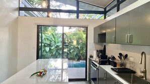 Eine moderne Küche mit großem Fenster, Edelstahlgeräten und Blick auf Grünfläche.
