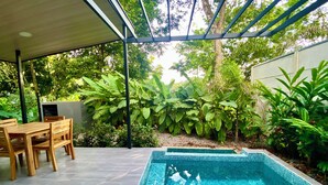 Eine überdachte Terrasse mit Pool, Holzmöbeln und üppiger Bepflanzung.