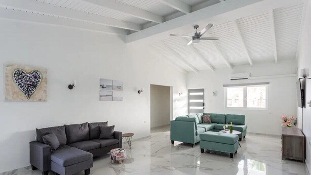 Un salon spacieux avec un grand canapé d’angle gris, un ensemble de canapés turquoise et un sol en marbre.