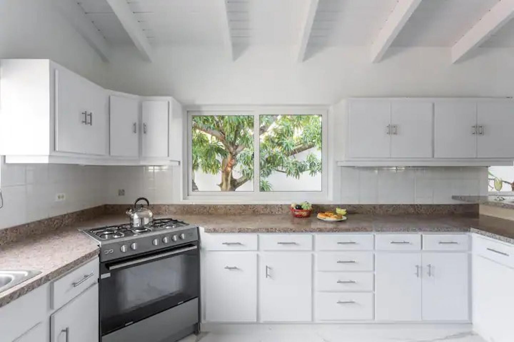 A modern kitchen with white cabinets, a gas stove, and a window with a view of trees.