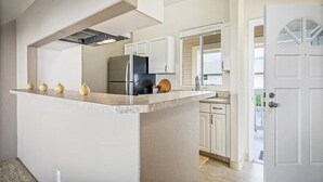 Een keuken met een centraal eiland, witte kasten, een koelkast en een deur met een raam.