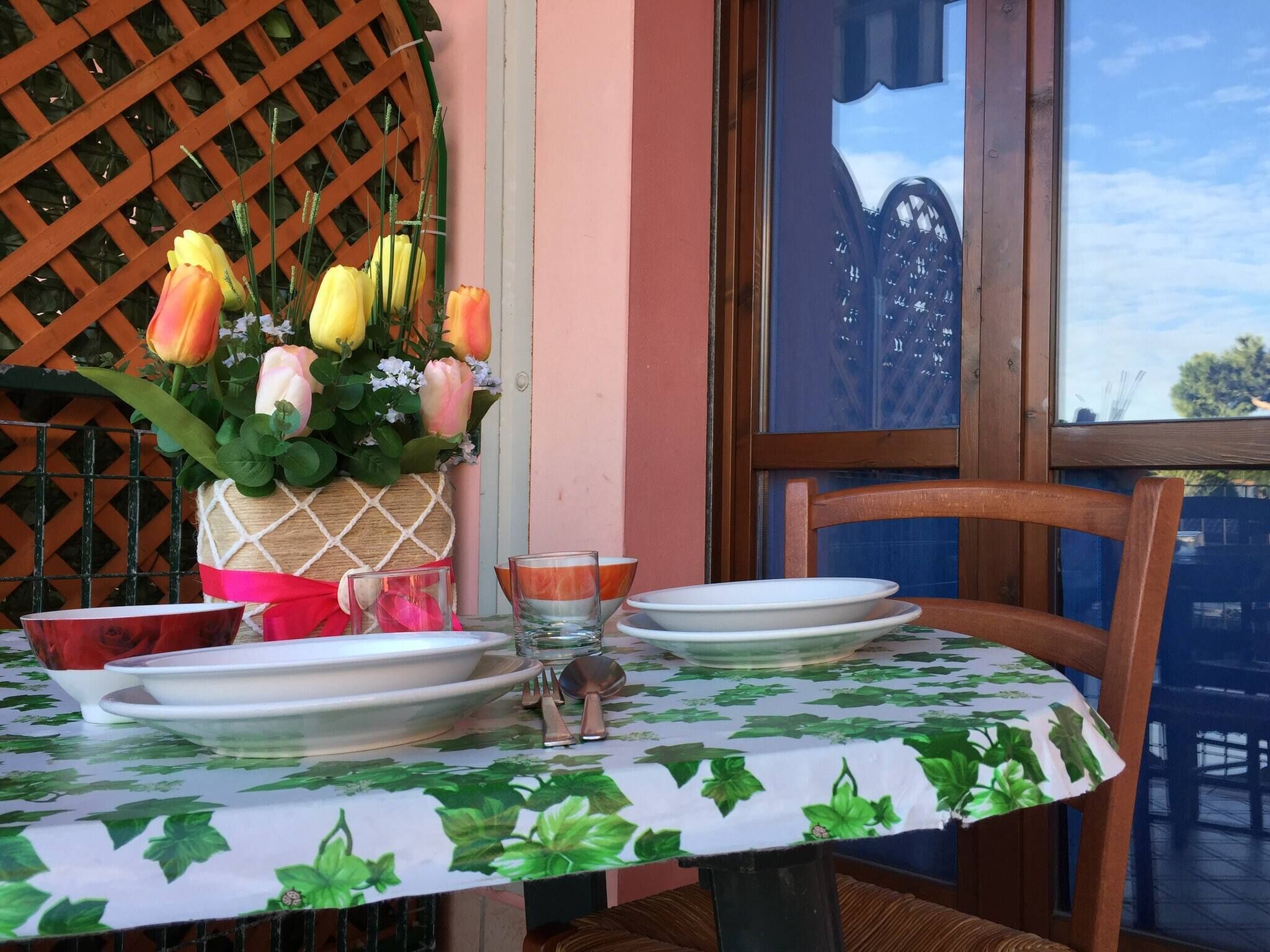 Uma mesa posta com pratos brancos, um copo e um vaso com tulipas amarelas e rosas.