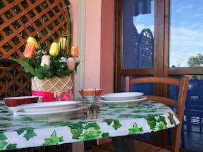 A table set with plates, a glass, and a vase of flowers, with a lattice and a window in the background.