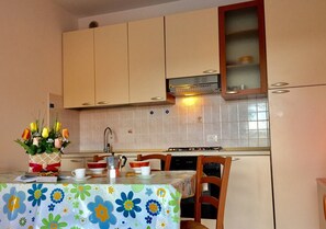A kitchen with beige cabinets, a tiled backsplash, a stove, and a dining table with a floral tablecloth.