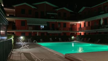 Piscina com espreguiçadeiras e um edifício com varandas ao fundo.