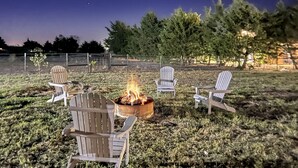 Un espacio al aire libre con asientos nocturnos, una fogata rodeada de sillas Adirondack.