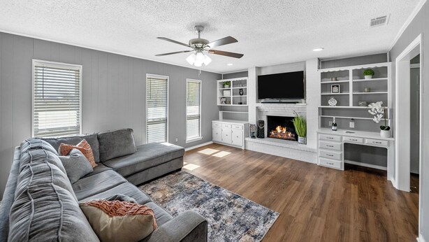 Una sala de estar moderna con un sofá gris, una chimenea, un televisor y un ventilador de techo.