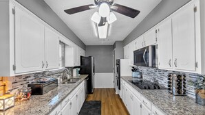 Una cocina moderna con armarios blancos, encimeras de granito, un refrigerador negro, un microondas y un ventilador de techo.