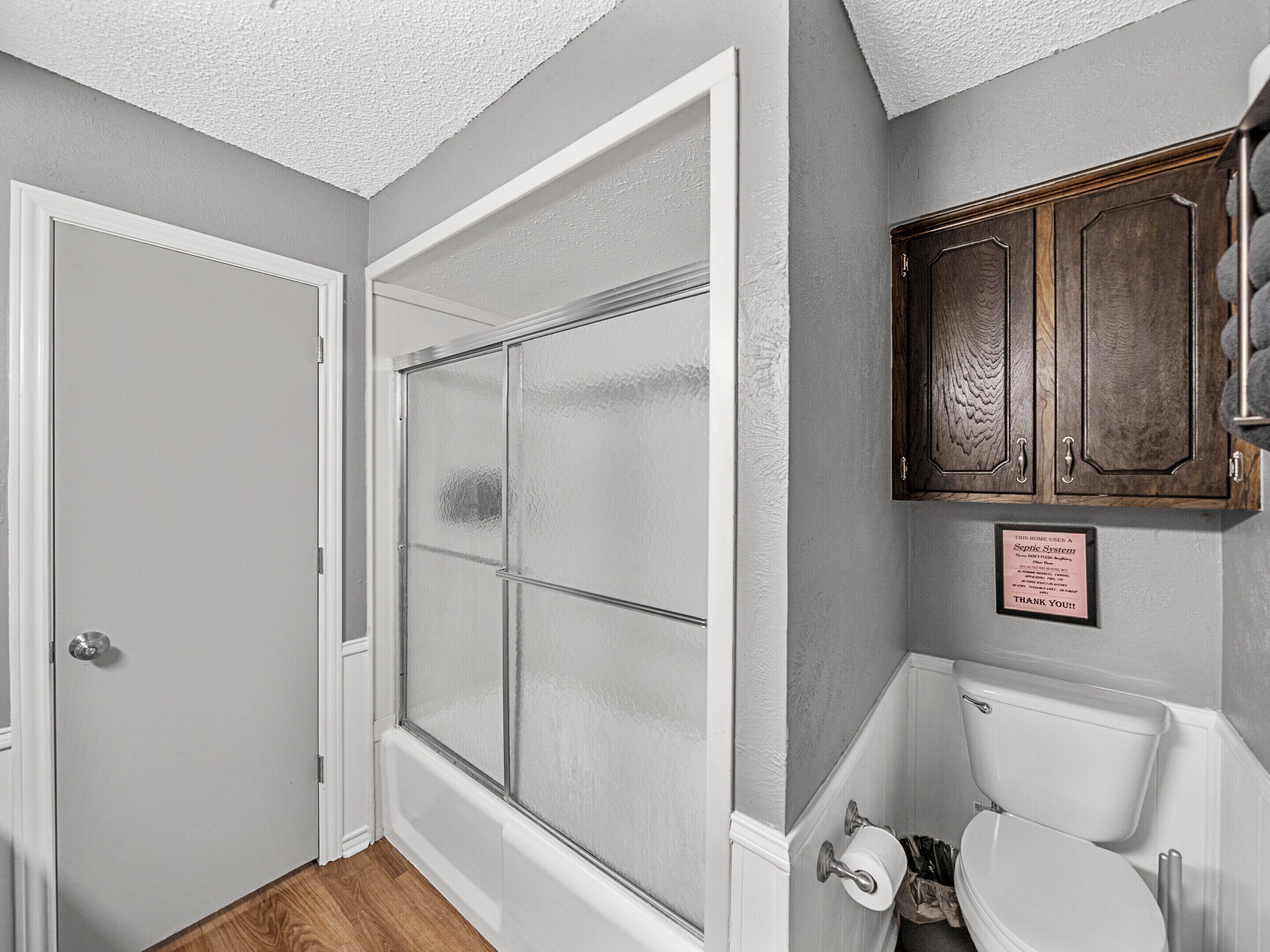 A bathroom with a toilet, a cabinet, and a frosted glass shower door.