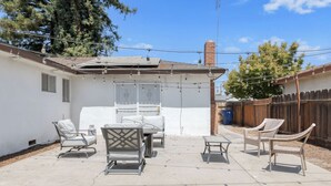 A backyard patio with a table and chairs, a covered seating area, and a wooden fence.