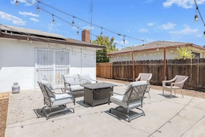 A backyard patio with outdoor furniture, string lights, and a wooden fence.