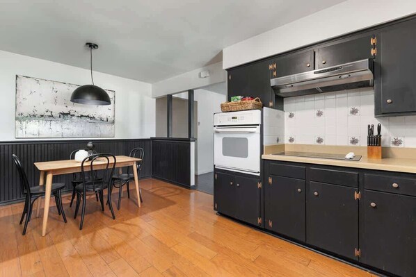 A modern kitchen with black cabinets, a wooden dining table, and a pendant light.