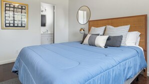 A bedroom with a large bed, a bedside table, a mirror, and a framed artwork on the wall.