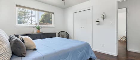 Un dormitorio con cama, ventilador de techo, ventana, puerta y una pequeña planta en maceta.