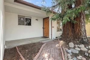 A house with a wooden door, a small porch, and a large tree in front.