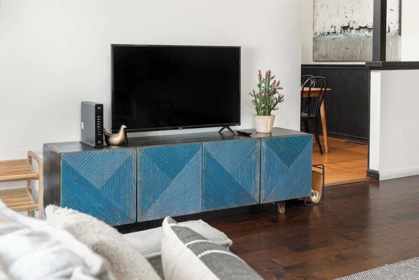 Un salon moderne avec un téléviseur à écran plat posé sur un meuble orné de motifs bleus, une petite plante et une chaise en bois.