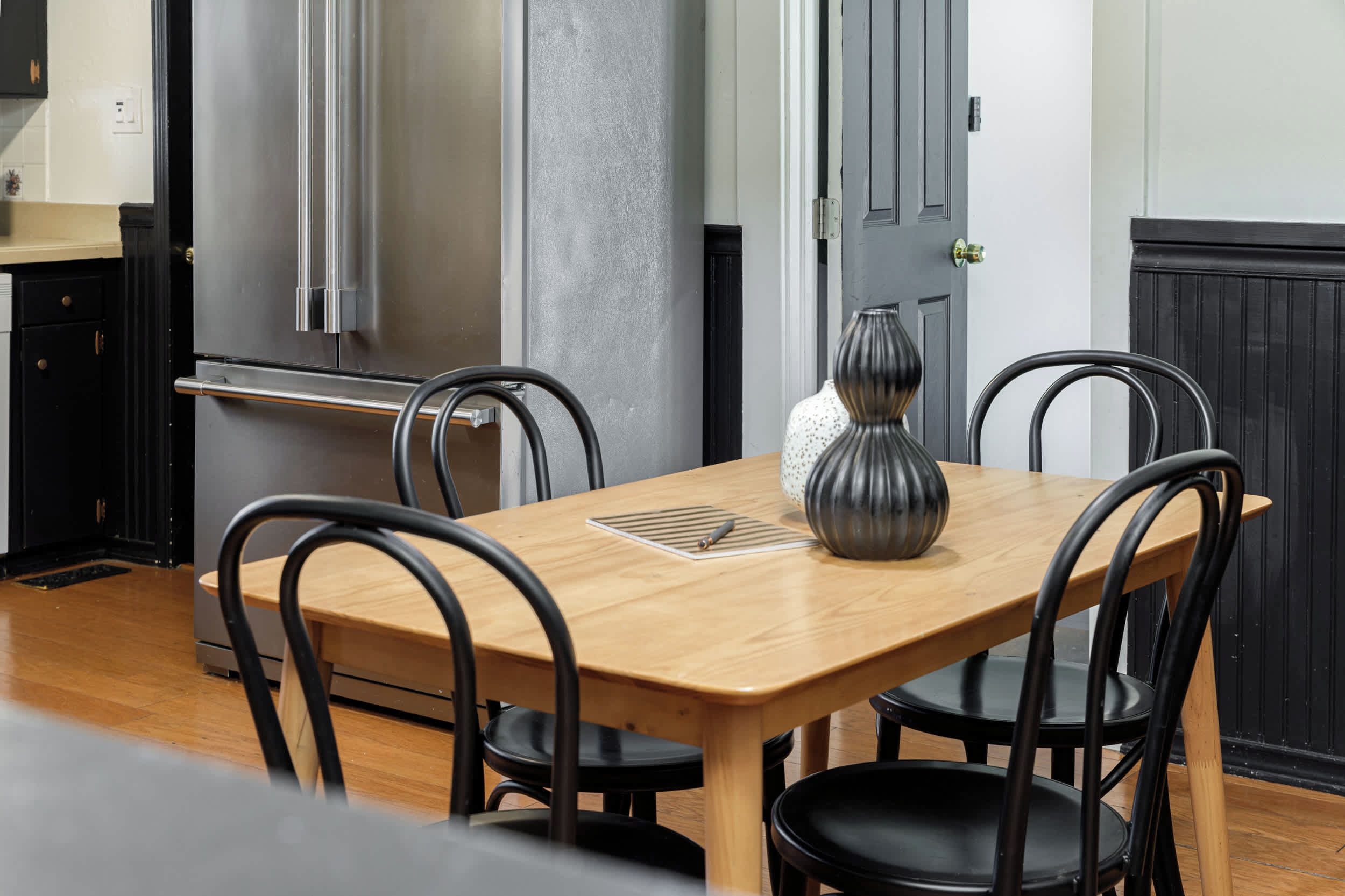 Un coin repas avec une table en bois et quatre chaises, un vase et une porte dotée d’une poignée.